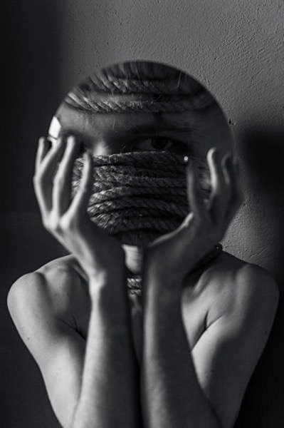 Person bound by rope looking into mirror — representing the experience of anxiety