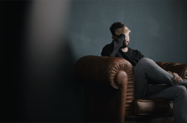 Man sitting on couch with hand to forehead